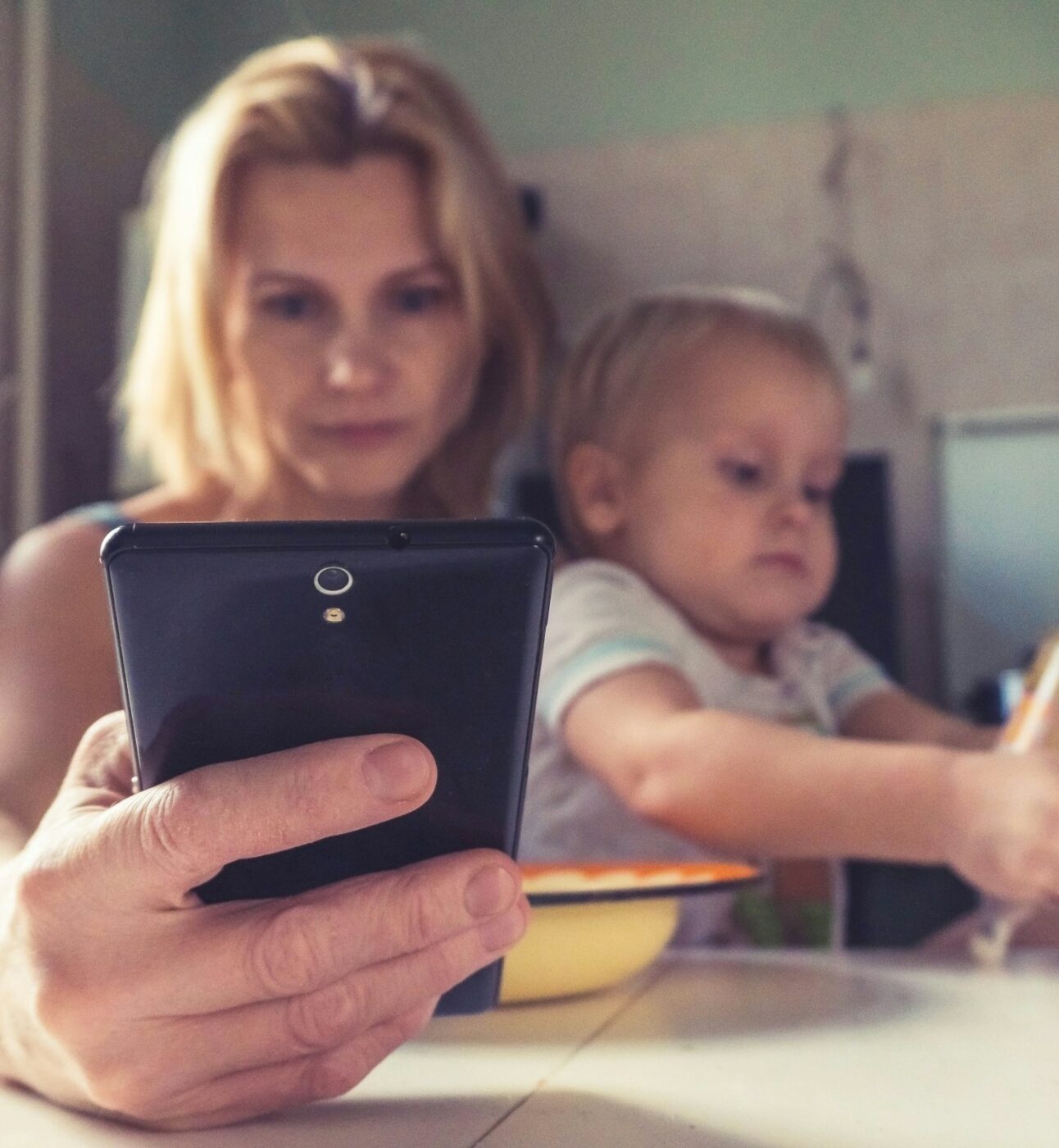 Mother looking at phone while holding children at the table