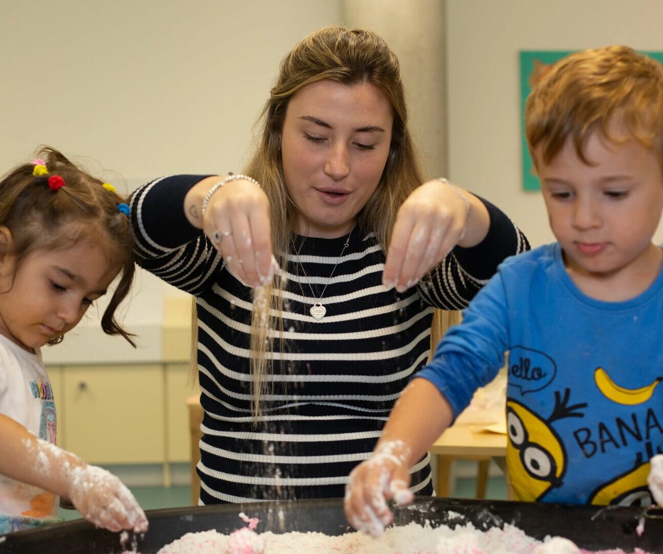 Teacher and two children play with sand in a tray